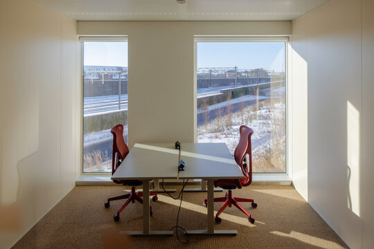 An empty office with two desks and office chairs with a view on train tracks and snow on the ground.