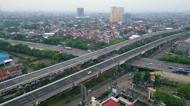 Aerial view of busy toll road crossing dense city area with bridges, cars, and urban housing, showing transport flow and city growth.
