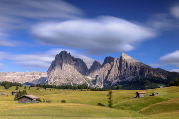 View over the alpine meadows with mountain cabins towards the Langkofel group with the peaks of Langkofel and Plattkofel on the Seiser Alm, Dolomites, South Tyrol, Italy.