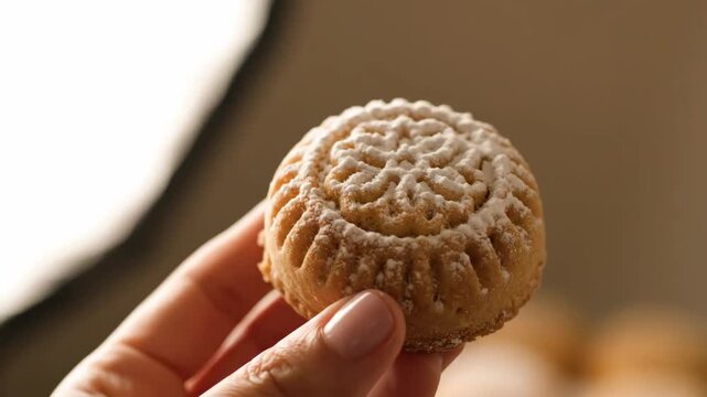 A perfectly baked sweet cookie held gently between two fingers decorated with intricate floral pattern showcasing culinary artistry and delicious homemade treat
