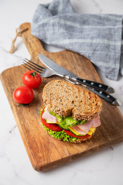 Sandwich with ham, cheese, lettuce, vegetables and seeded bread on a wooden board