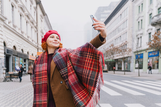 Urban portrait of confident woman taking selfie on city street