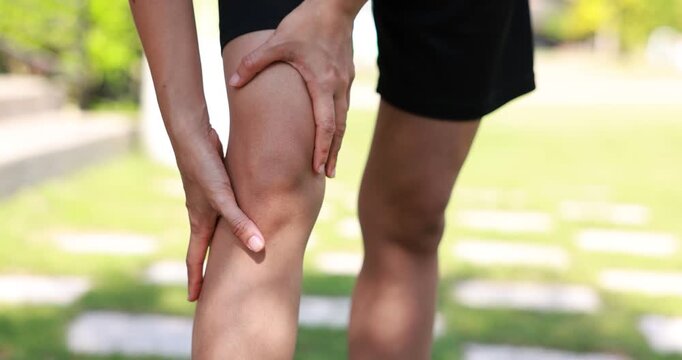 4K slow motion close up of hands rubbing injured knee. Athlete suffering from joint pain or leg inflammation while running in park. Healthcare and sports injury concept.