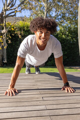 Fitness enthusiast performing push-ups on wooden deck near grass lawn