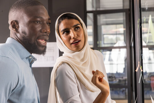 Diverse coworkers in business attire reviewing project diagrams on glass board in office - Powered by Adobe