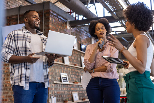 Diverse coworkers discussing project in loft office with laptop smartphone tablet - Powered by Adobe