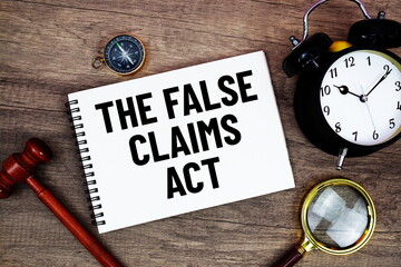 The False Claims Act message written on notepad with alarm clock, wood gavel and magnifying glass flat lay on wooden background
