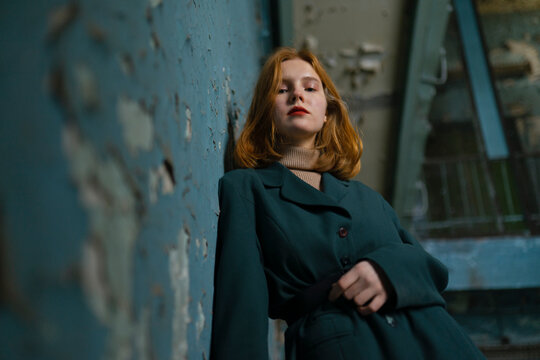 Red-haired teenager in green jacket feeling melancholy by peeling wall