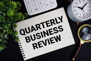 QBR Quarterly Business Review text written on notepad with alarm clock, magnifying glass and calculator on black background