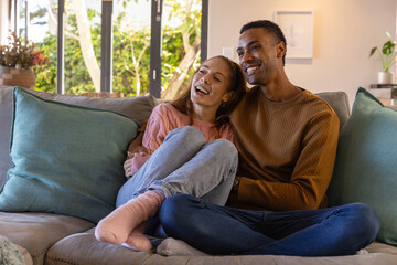 Obraz premium Couple sitting on couch at home by glass doors with green cushions, wearing sweaters