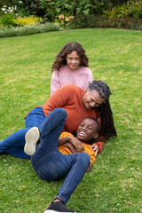 Fototapeta premium African american family tickling on green lawn in backyard garden with plants