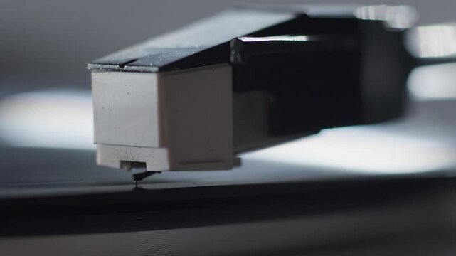A close-up of the needle of a vinyl record player as it plays a record and later stops playing the record.