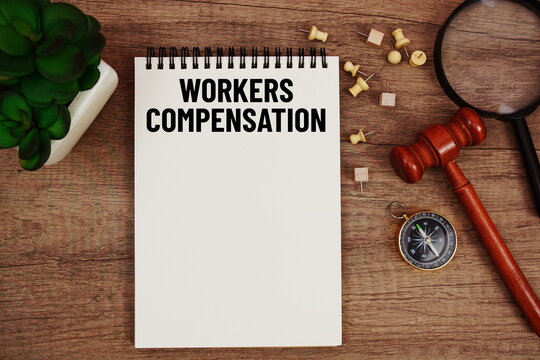 Workers Compensation message written on notepad with wood gavel and magnifying glass flat lay on wooden background