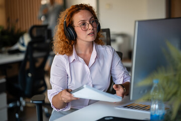 Focused young businesswoman with headphones working in modern office