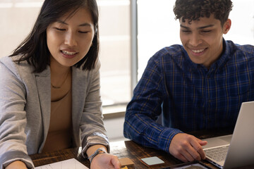 Diverse coworkers in business casual collaborating over printed documents and laptop in office