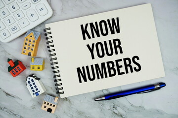 Know Your Numbers text written on notepad with house model and calculator on marble background