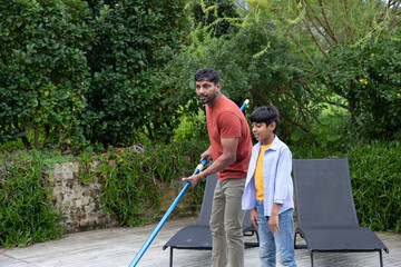 Indian father with son standing on wooden deck by pool skimming water with long-handled net © wavebreak3