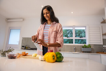 Indian woman chopping vegetables on wooden cutting board at kitchen island with peppers, olives