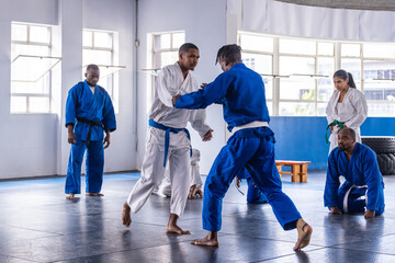 Diverse martial arts classmates in gis practicing grappling on mats in dojo with large tire