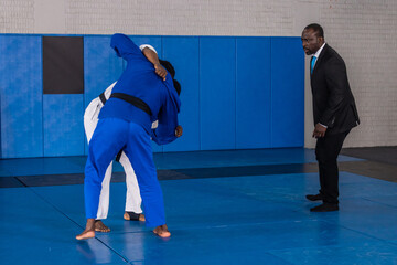 African american instructor supervising diverse male students grappling on mats in dojo in gis