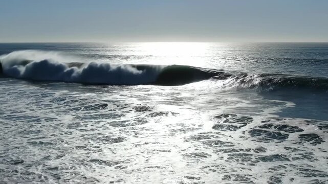 A powerful wave crashes under the bright sunlight reflecting off the ocean s surface The vast expanse of water stretches towards the horizon under a clear sky