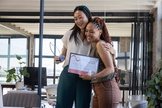Diverse female coworkers celebrating success in open-plan office holding trophy and certificate - Powered by Adobe