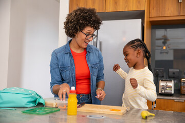 African american mother with daughter arranging snack container with juice bottle on kitchen island