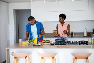 Diverse couple chopping vegetables on cutting board and cooking with frying pan on kitchen island