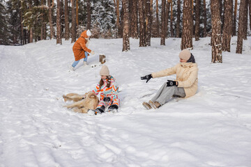 Two teenagers and adult woman playing with Golden Retriever dog in snowy pine forest during winter family outdoor leisure and peaceful nature walk