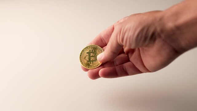 A man's hand plays with a gold bitcoin coin, spinning it on a white surface. Concept of financial gains. Virtual economy and cryptocurrency. Cryptoeconomics. 4k video