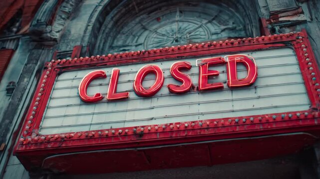 A red and white signboard with the word CLOSED displayed prominently in red letters is attached to a building facade with a large arched window and stonework details in the daytime