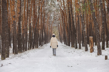 Teenage girl walking alone along snowy pine forest corridor, quiet winter path with tall trees, peaceful outdoor lifestyle, cold season travel and calm nature atmosphere