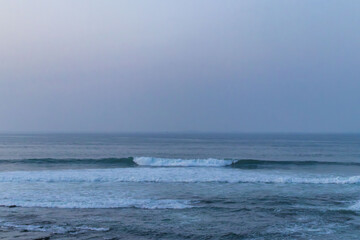 An Atlantic beach with a soft sunset with reflections of the sky in the water and people on the shore.