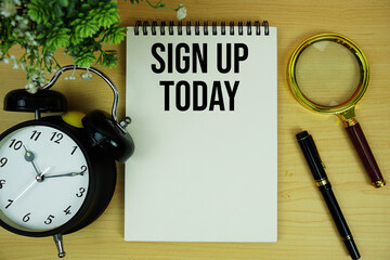 Sign Up Today text written on notepad with alarm clock and magnifying glass flat lay on wooden background