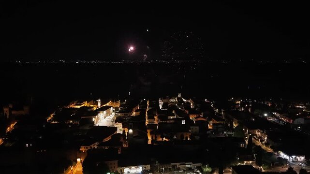 Aerial drone video of Lazise, Italy, with summer fireworks reflecting on Lake Garda. Historic center and lakeside town captured in 4K.