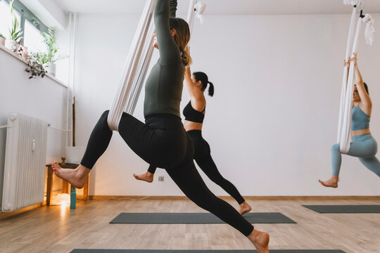 Group practicing aerial yoga with hammocks in indoor studio