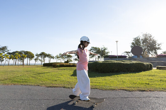 Asian girl skateboarding alone outdoors while wearing a safety helmet, showing child safety, outdoor activity, and active childhood lifestyle.