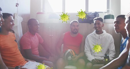 Animation of covid-19 cells icons over team of diverse male soccer players discussing in locker room - Powered by Adobe