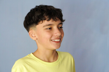 Portrait of a smiling preteen boy with freckles wearing a yellow T-shirt and blue background