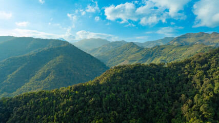 Fototapeta premium Breathtaking aerial view of lush green tropical mountains under a clear blue sky with white clouds, scenic nature landscape and eco-tourism adventure concept from drone.concept nature