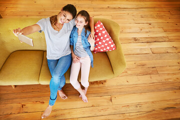 Above, hug and selfie of daughter with mom on sofa in home living room together for profile picture. App, love or photograph with girl and single parent woman embracing in apartment for social media