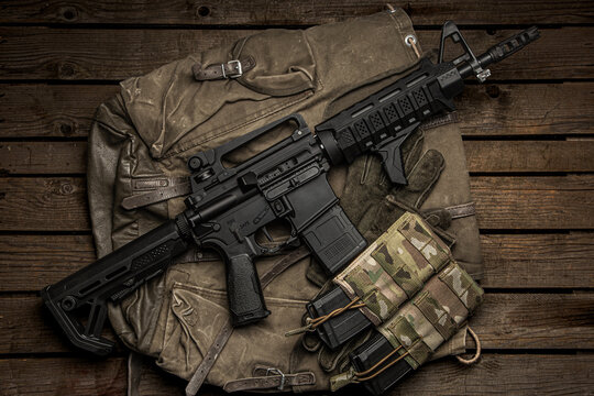 Black rifle, tactical gear, and camo pouches on a vintage canvas bag and wooden back