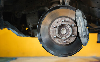 Automotive Safety and Maintenance, Close-up of car disc brake rotor and caliper assembly on wheel hub with suspension detail in auto repair garage with hydraulic lift, Engineering Mechanism
