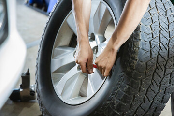 Auto mechanic technician holding car wheel and using tool to inspect tire valve or center cap in garage service workshop, Quality control, Manual labor, Skill Expertise, Heavy duty Industrial concept