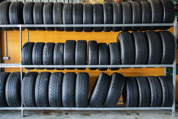 Rows of new black car tires with deep tread pattern stacked on metal rack in auto parts store warehouse inventory, Tire shop, Auto parts store, Inventory Stock Supply Buying tires, Business Commerce © Sumala
