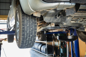 Low angle view of pickup truck undercarriage and front suspension on hydraulic lift with oil drain tank ready for engine oil change service in garage, Engine maintenance, Auto repair, Car service © Sumala