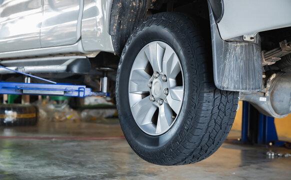 Rear wheel of dirty off-road pickup truck on hydraulic lift showing mud flap and leaf spring suspension in auto repair garage, Auto repair shop, Car service, Truck maintenance, Off-road vehicle