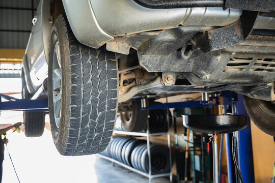 Low angle view of pickup truck undercarriage and front suspension on hydraulic lift with oil drain tank ready for engine oil change service in garage, Engine maintenance, Auto repair, Car service