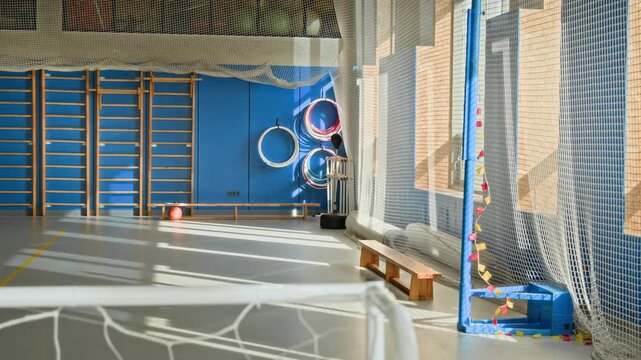 Tilt up shot of empty indoor gym in school lit by sunlight with soccer gate in foreground and protective netting on windows, no people, copy space