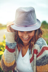 Fototapeta premium Smile, woman and sunhat outdoor for travel, spring adventure and holiday trip. Happy, female person and explore nature with floral daisies, sunshine and fresh air on vacation getaway in countryside